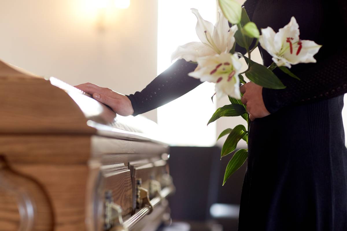 man holding a bouquet of flowers and touching the coffin
